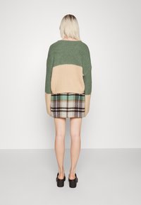 Gebreide trui in groen en beige met een geruite rok, voorzien van een ontspannen pasvorm, textuurafwerking en contrasterende kleurvlakken aan de bovenkant.