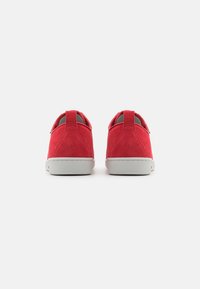 Zapatillas de ante rojo con diseño de corte bajo, detalles en gris y suela de goma. Incluyen lengüetas en el talón para facilitar su colocación.