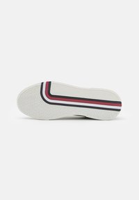 Suola di sneaker bianca con grip testurizzato, caratterizzata da un design a strisce nere, rosse e bianche. Forma arrotondata con superficie piatta.