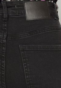 Os jeans de denim pretos apresentam uma textura lisa, um ajuste elegante e um patch de couro com a marca "Denim Project" na cintura.