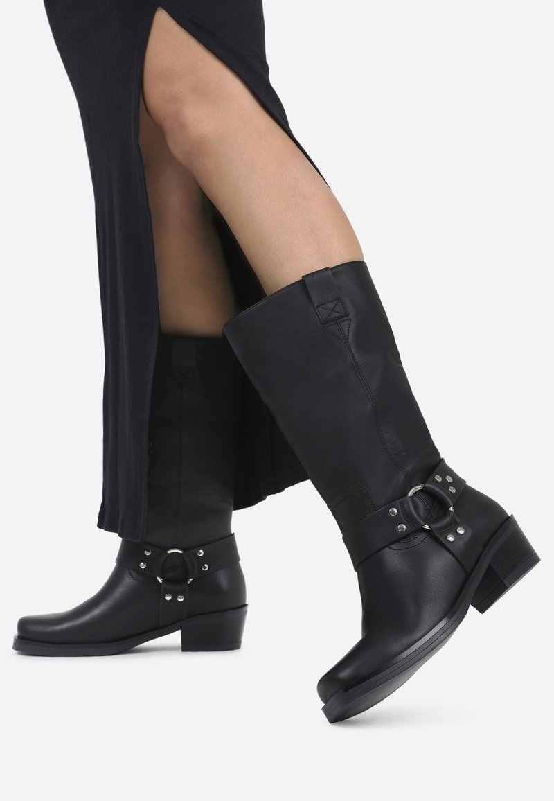 Czarne skórzane wysokie botki na kolano z okrągłym noskiem, masywnym niskim obcasem i ozdobnym paskiem z klamrą oraz srebrnymi ćwiekami.