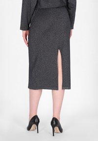 Grauer, strukturierter Bleistiftrock mit einem seitlichen Schlitz, aus einem glänzenden Stoff gefertigt. Kombiniert mit schwarzen High Heels, die eine elegante Silhouette zeigen.