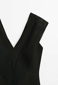 Haut sans manches noir avec un large col en V et des détails en maille texturée le long de l'encolure et des épaules.
