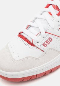 Baskets en cuir blanc avec accents rouges, languette rembourrée, embout en suède, panneaux en maille et semelle en caoutchouc texturé. Présente un logo "550".