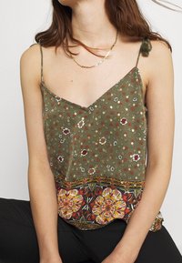 Grön blommig linne med tunna axelband, med en kontrasterande mönstrad fåll i nyanser av rött, gult och svart. Lättviktig tyg.