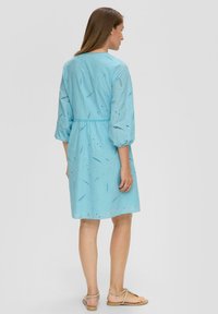 Helles blaues Kleid aus strukturiertem Stoff mit Stickerei. Verfügt über Dreiviertelärmel, eine taillierte Taille und einen ausgestellten Rock.