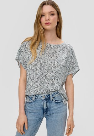 Kurzarm-Oberteil mit floralem Muster in Hellblau und Weiß, aus weichem Stoff, mit lockerer Passform und rundem Halsausschnitt. Kombiniert mit blauen Jeans.