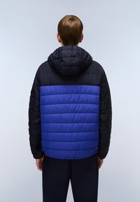 Polstret jakke med en blå torso og sorte ærmer, der har en hætte og vandret quiltning. Materialet virker glat og let.