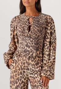 Leopard print blouse with a shirred, textured bodice and puff sleeves. Keyhole neckline with tie detail. Coordinating animal print pants.