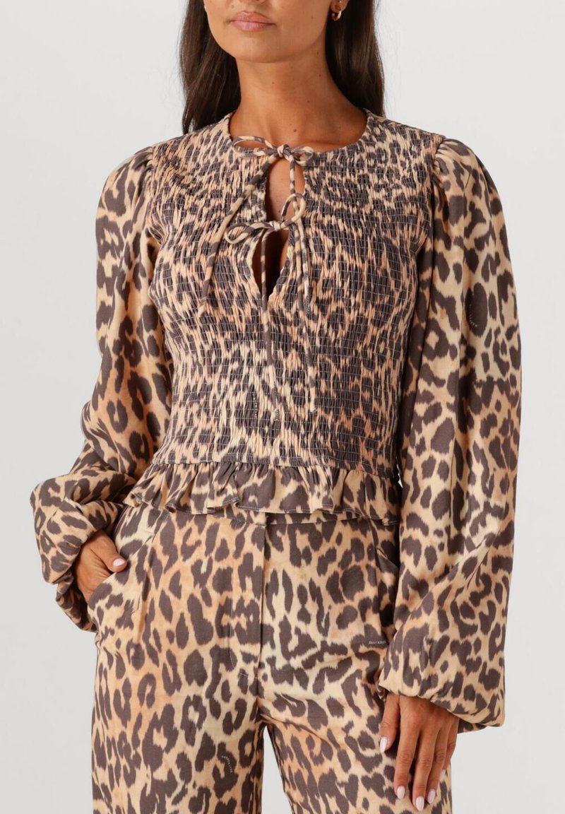 Leopard print blouse with a shirred, textured bodice and puff sleeves. Keyhole neckline with tie detail. Coordinating animal print pants.
