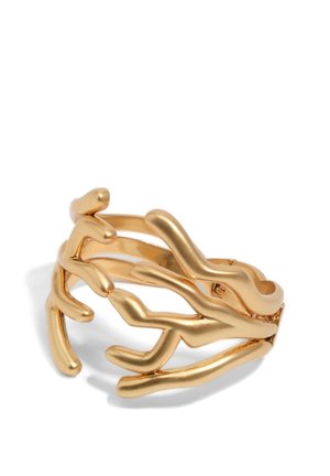 Złoty pierścionek o otwartym wzorze przypominającym abstrakcyjne gałęzie koralowca, polerowane wykończenie, rzucający miękkie cienie na białym tle.