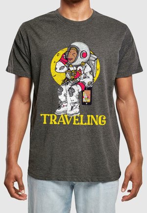 Szary t-shirt z rysunkowym astronautą trzymającym napój, na żółtym okrągłym tle oraz napisem "PODRÓŻUJĄC" w pogrubionych żółtych literach.