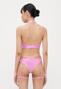 Pink lingerie set featuring lace accents, a strapless bra, and matching garter belt with cross straps and adjustable suspenders.