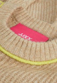 Maglione beige in maglia caratterizzato da una texture a coste, scollo rotondo e un brillante accento giallo. L'etichetta interna recita "JUXX" su uno sfondo rosa.