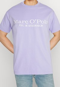 T-shirt en coton lilas avec un col rond et des manches courtes, comportant un texte brodé blanc indiquant "Marc O'Polo EST. À STOCKHOLM."