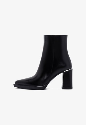 Zwarte enkelboot gemaakt van soepel leer met een spitse neus. Heeft een chunky vierkante hak en zilveren accenten langs de basis.
