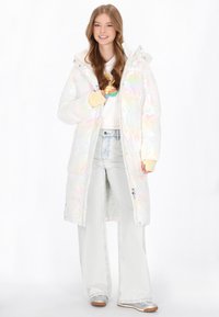 Iridescens, hosszú puffernadrág kapucnival, cipzáras zsebekkel és texturált felülettel. Egy fehér pulóverrel és világoskék farmernadrággal párosítva.