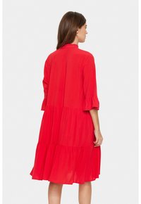 Robe rouge, longueur genoux, en tissu léger. Dotée d'un design à étages, de manches évasées trois-quarts et d'un col à volants.