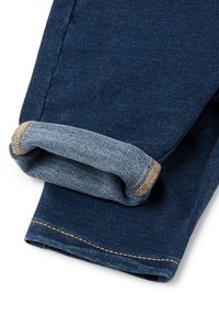 Srolované tmavě modré džíny s odhalenou vnitřní světlejší tkaninou a oranžovým šitím na okraji.