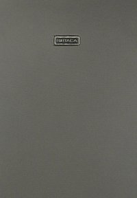 Superficie de tela gris con una pequeña placa rectangular metálica que muestra el nombre de la marca "ITACA" centrado cerca de la parte superior.