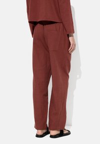 Pantalony szerokie w kolorze rdzy, wykonane z miękkiego materiału, z elastycznym paskiem w pasie i jedną kieszenią z tyłu.