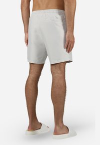 Bañador blanco con una cinturilla elástica, que presenta un bolsillo trasero. Textura suave. Combinado con unas sencillas sandalias blancas sin hebilla.