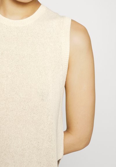 Beige kötött ujjatlan felső bordás dekoltázzsal és laza fazonnal, amely puha textúrával és könnyű anyaggal rendelkezik, tökéletes meleg időjárásra.