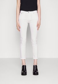 Jeans blancos ajustados con una cintura de altura media, que cuentan con cinco bolsillos, costuras sutiles y un acabado limpio. Combinados con botas de tacón negras.