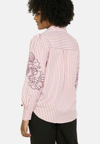 Pruhovaná ružová blúzka s dlhými rukávmi, so získavaným kvetinovým vyšívaním na rukávoch, gombíkovými manžetami a zaobleným lemom.