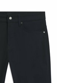 Mörka jeans i denim med en mjuk textur, utrustade med en klassisk design med fem fickor, en silverfärgad metallknapp och diskreta sömmar som accenter.