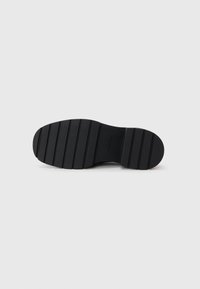 Suola in gomma nera con superficie texturizzata, caratterizzata da scanalature orizzontali per una maggiore aderenza e una forma arrotondata. Marchiata con "Calvin Klein" sul lato.