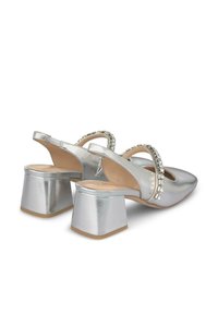 Scarpe slingback argento con punta affusolata, tacco a blocco e cinturino decorativo con strass. Finitura metallizzata liscia e design con schiena aperta.