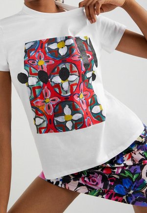 Valkoinen lyhythihainen t-paita, jossa on värikäs kukkakuosi, jossa on punaisia, keltaisia ja mustia yksityiskohtia. Pehmeää kangasta, rento leikkaus, peruspyöreä kaula-aukko.