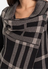 Maglione lavorato a maglia in nero e beige con un motivo a quadri. Presenta un ampio collare drappeggiato e un dettaglio di bottoni alla scollatura.