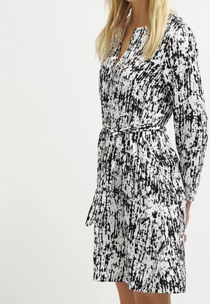 Robe à motifs noir et blanc avec une taille ceinturée, des manches longues et un col en V. Fabriquée dans un tissu lisse avec un imprimé texturé.