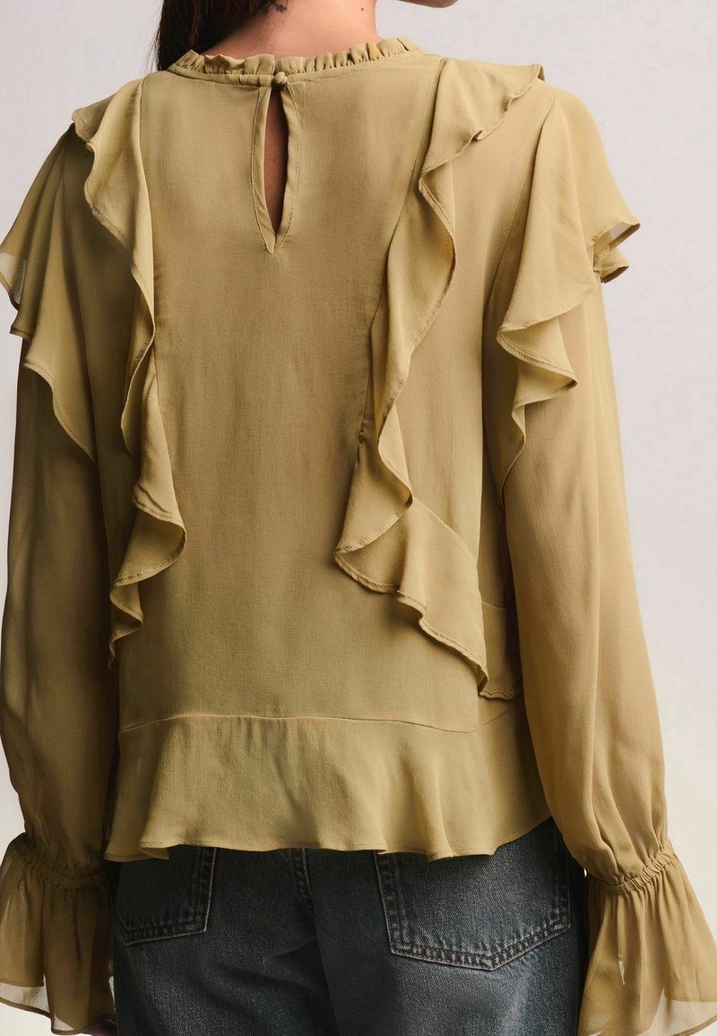 Blouse vert olive avec accents à volants, manches longues, dos fendu en forme de clé et tissu doux et léger. Caractérisée par des poignets froncés et un ourlet évasé.