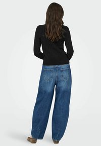Czarny prążkowany sweter w połączeniu z oversize'owymi niebieskimi dżinsami. Dżinsy mają luźny krój i dwie tylne kieszenie. Proste obuwie dopełnia stylizację.