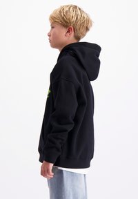 Zwarte hoodie met een kangoeroezak, zachte textuur, groene grafische details en geribbelde manchetten, gedragen bij lichtblauwe jeans.