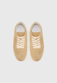 Sneakers in suede beige con lacci color crema, punta arrotondata, tomaia texturizzata e branding sottile sul lato. Suola piatta in gomma.