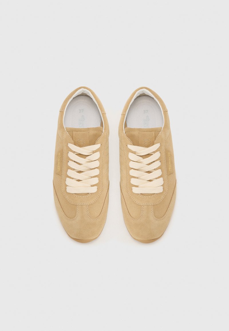 Beżowe zamszowe trampki z kremowymi sznurówkami, okrągłym noskiem, teksturowaną cholewką i subtelnym logo po boku. Płaska gumowa podeszwa.