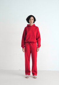 Compleu roșu dintr-un material moale, format dintr-un hanorac cu glugă și buzunar frontal, împreună cu pantaloni cu talie elastică și șnur.
