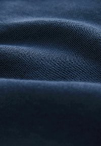 Granatowa tkanina o teksturowanym splocie, charakteryzująca się miękkim układaniem i subtelnym połyskiem, tworząca delikatne fale i gradienty w materiale.