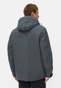 Grijze jas met capuchon, met een gladde textuur en een reflecterende strip op de achterkant. Het ontwerp omvat verstelbare koorden en manchetten.