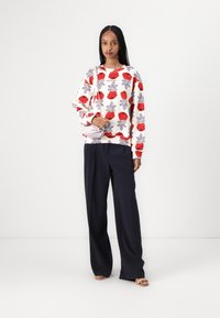 White sweatshirt featuring red and purple rose patterns, paired with high-waisted, wide-leg navy trousers. Model holding a light gray bag.