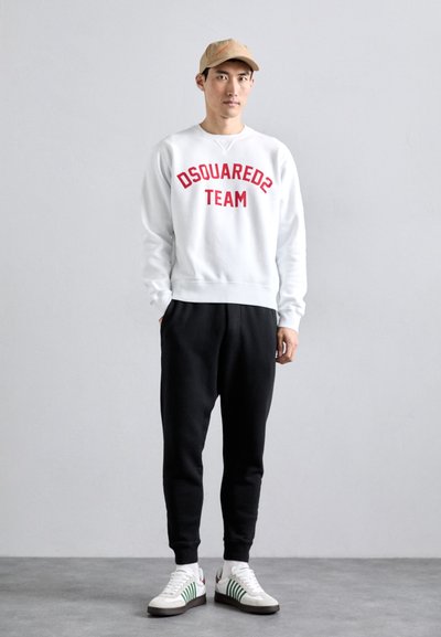 Valge sviiter, millel on kirjas "DSQUARED2 TEAM" punasega, mustad trennipüksid ja valged sneakersid roheliste triipudega. Igapäevane riietus, minimaalne disain.