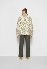 Quilted jacket in cream with green floral pattern, paired with dark green trousers and light footwear. Features a mandarin collar and relaxed fit.