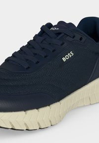 Baskets en mesh bleu marine pour homme avec logo « BOSS » blanc sur le côté et semelle épaisse blanche texturée, avec lacets bleu marine et col rembourré.