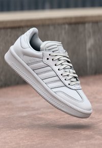 White leather sneaker with three gray stripes, padded tongue, and textured sole. Features a smooth finish and lace-up design.