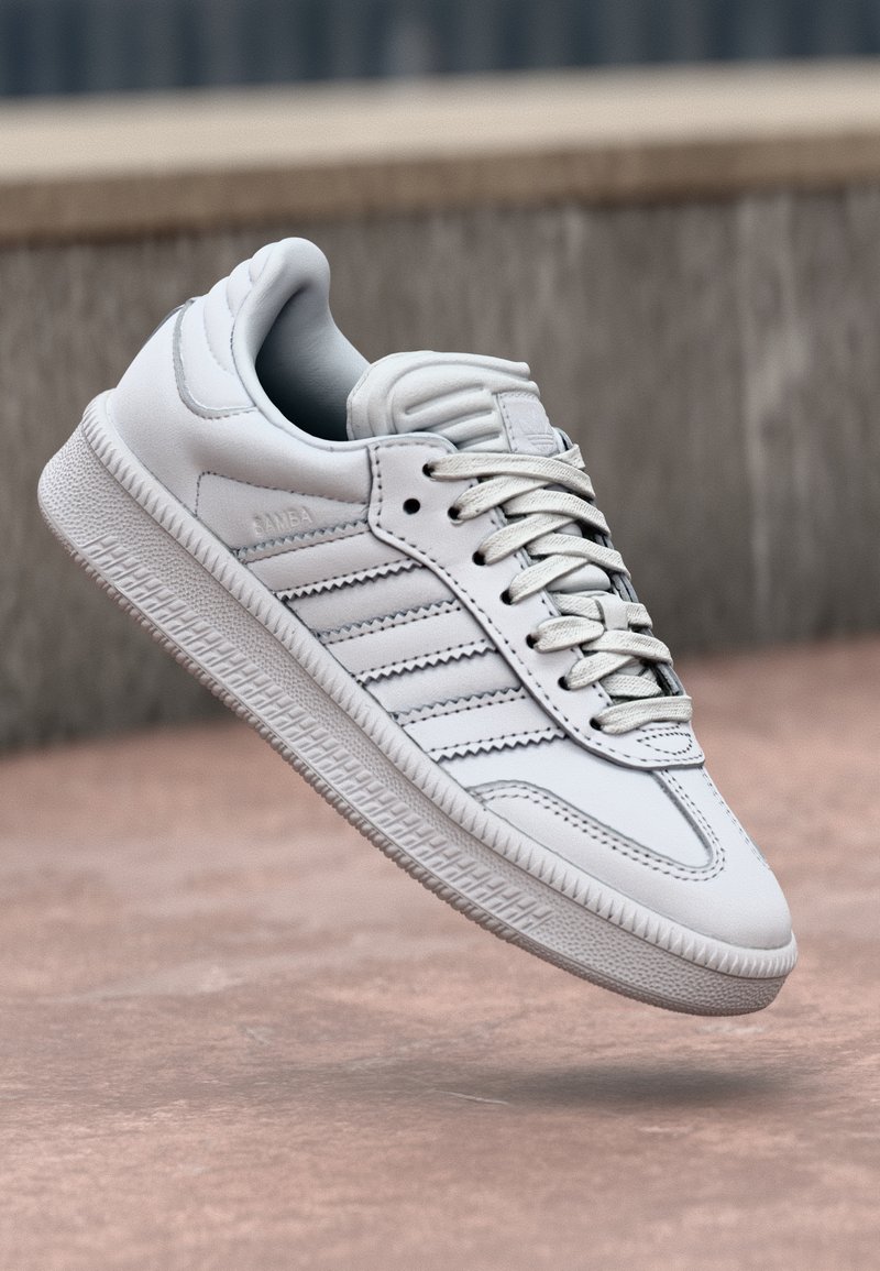 White leather sneaker with three gray stripes, padded tongue, and textured sole. Features a smooth finish and lace-up design.
