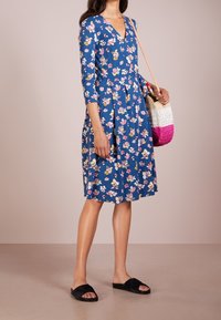 Blå blommig klänning med V-hals, trekvartärmar och plisserad kjol. Kombinerad med svarta halksandaler och en vävd handväska.